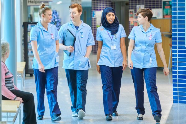 Vier Pflegekräfte gehen nebeneinander auf einem Krankenhausflur.